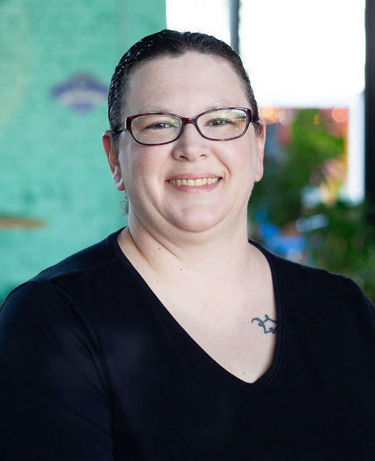 Portrait photo of editor and owner Kristen smiling with large windows and artwork in the background