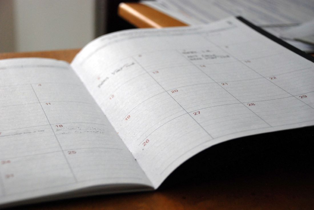 Photo of an open paper planner sitting on a desk. There are some items written on a few dates in the planner.