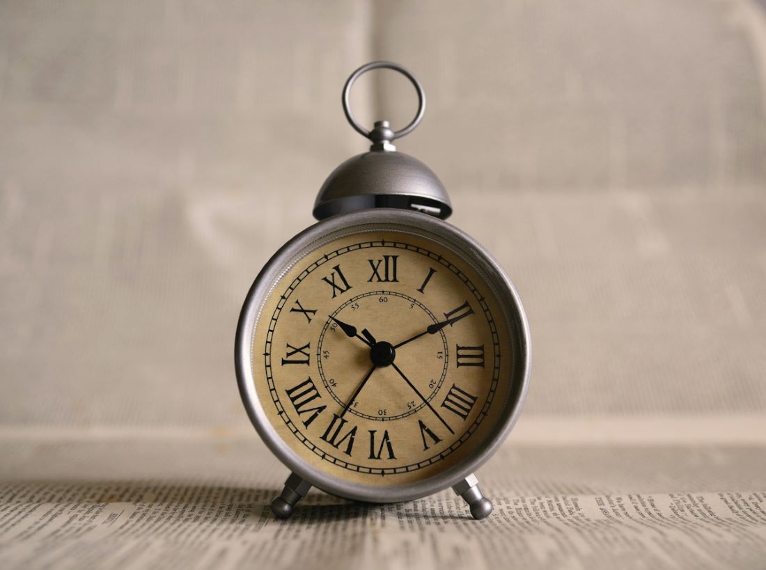 Closeup photograph of vintage alarm clock with a single bell on top and Roman numerals on its face.