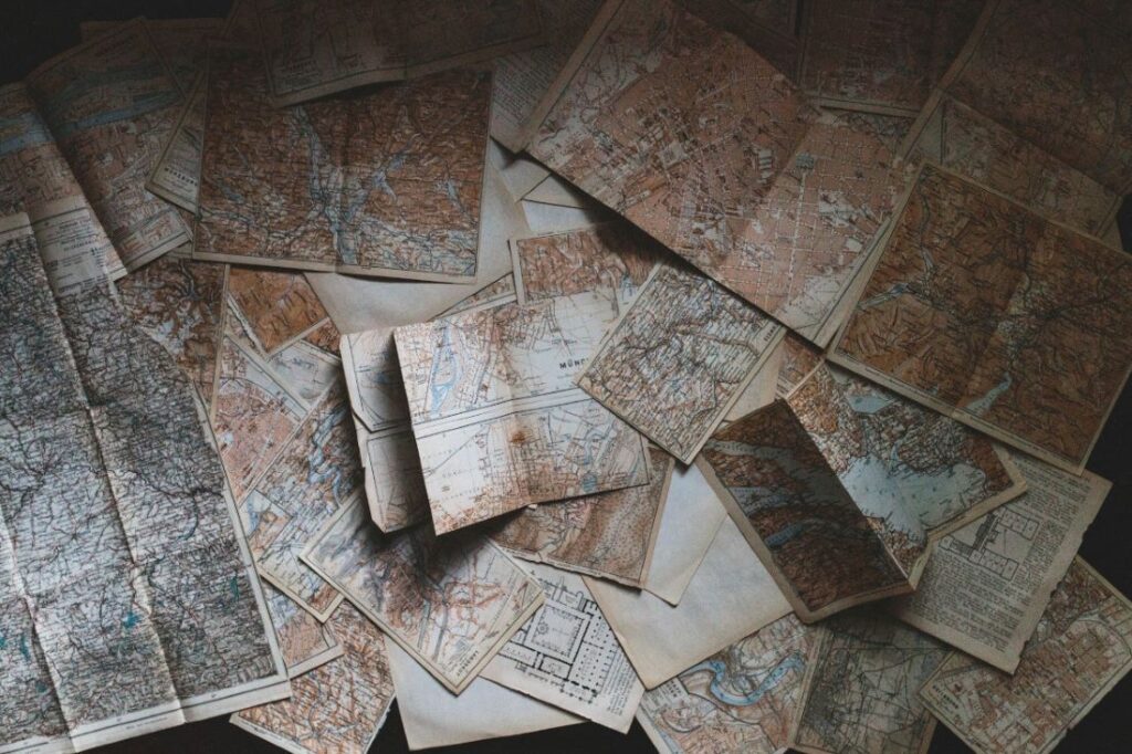 Assortment of vintage road maps piled haphazardly on a table.